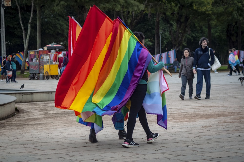 a couple of people walking down a street holding a rainbow flag