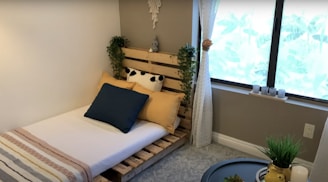A small bedroom nook with a floating shelf, geometric planters, and a comfy bed dressed in neutral tones.