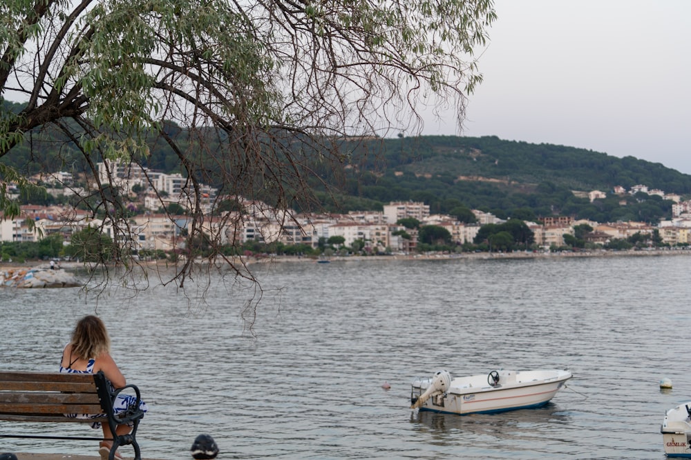 a woman sitting on a bench next to a body of water