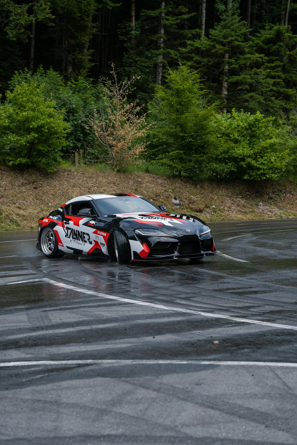 a black and red sports car driving on a wet road