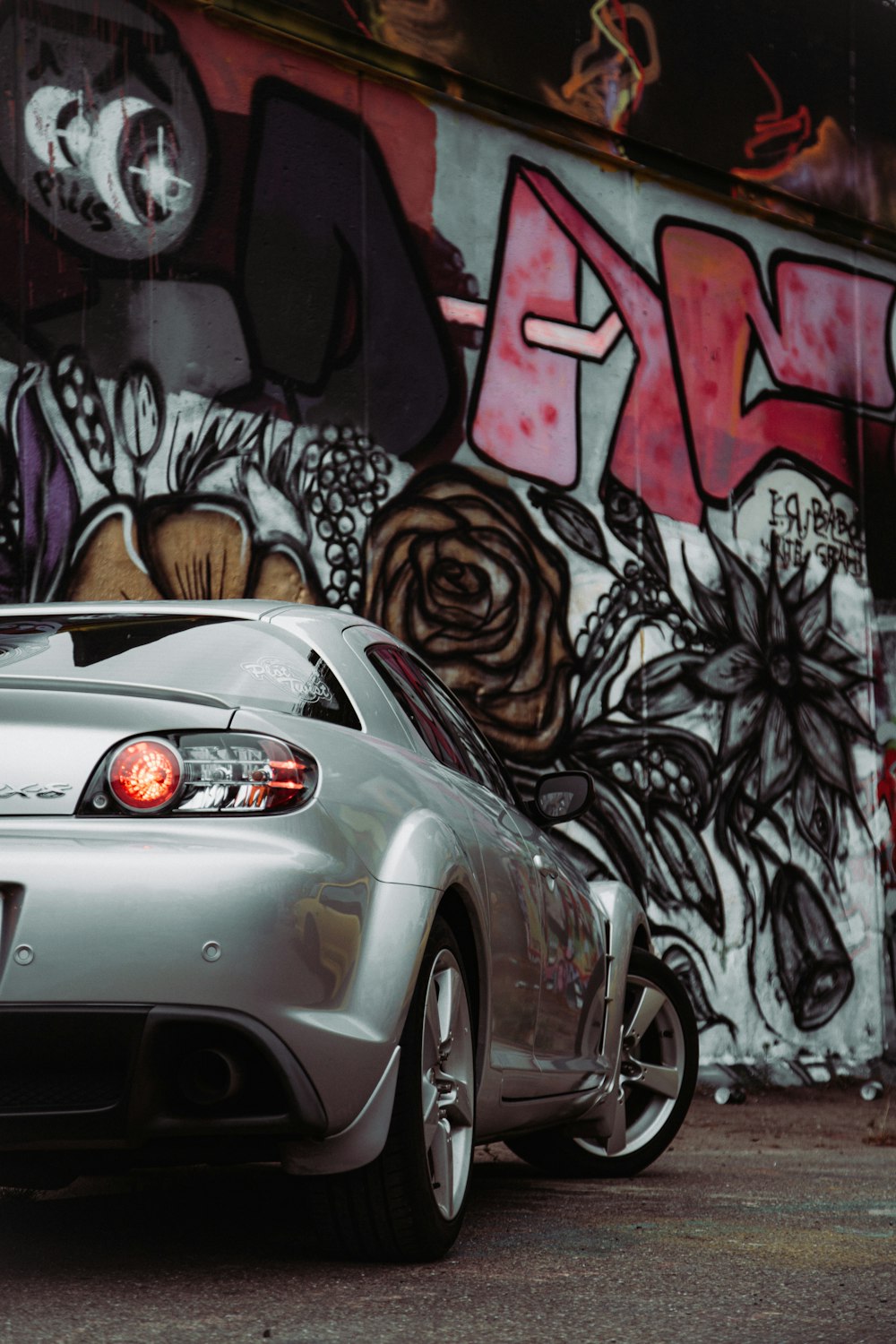 a silver sports car parked in front of a graffiti covered wall