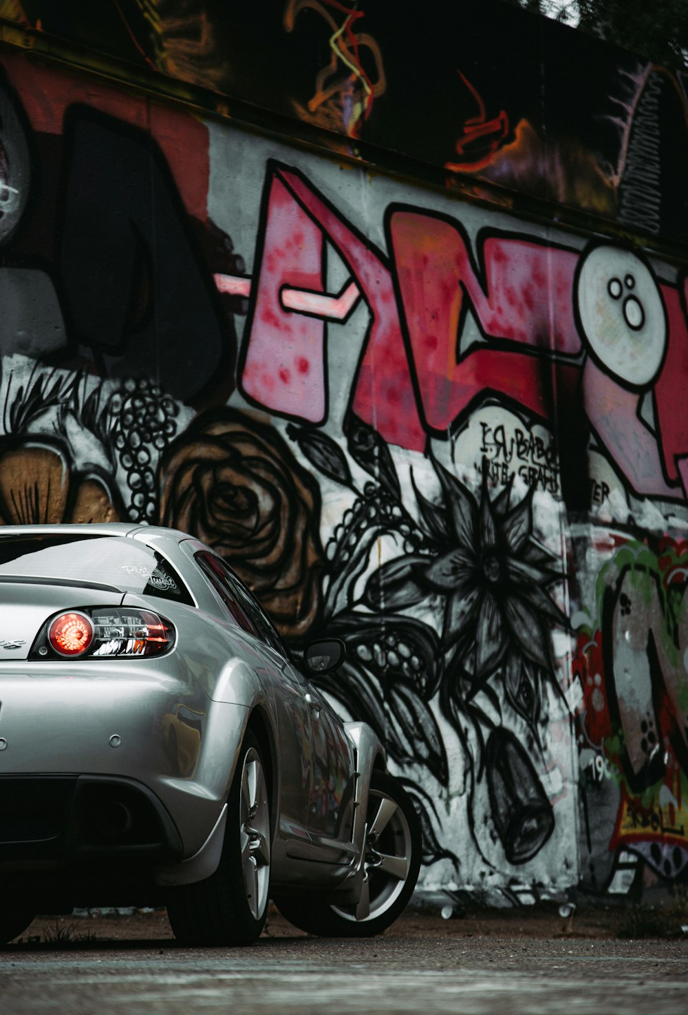 a silver sports car parked in front of a graffiti covered wall