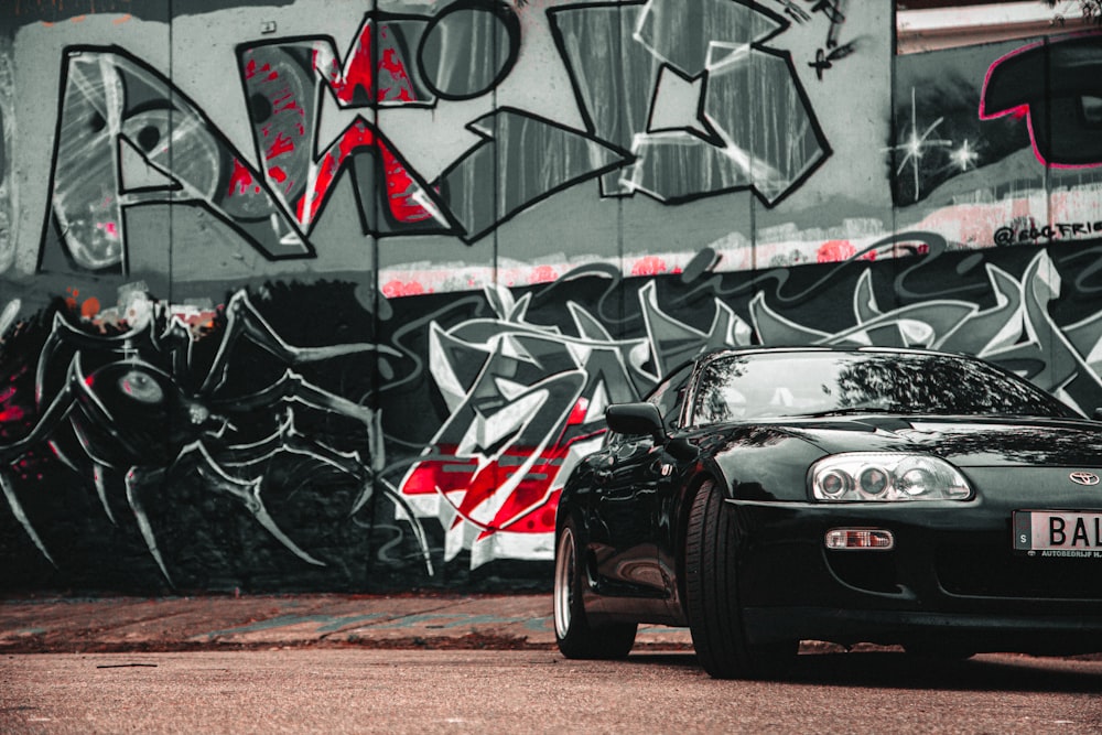 a black sports car parked in front of a graffiti covered wall