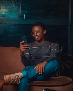 A young person smiling while working on a smartphone in a cozy, modern home setting.