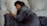 A person lies asleep on a bed, wrapped in a dark grey comforter. Their head rests on a light-colored pillow, and they appear peaceful and relaxed.
