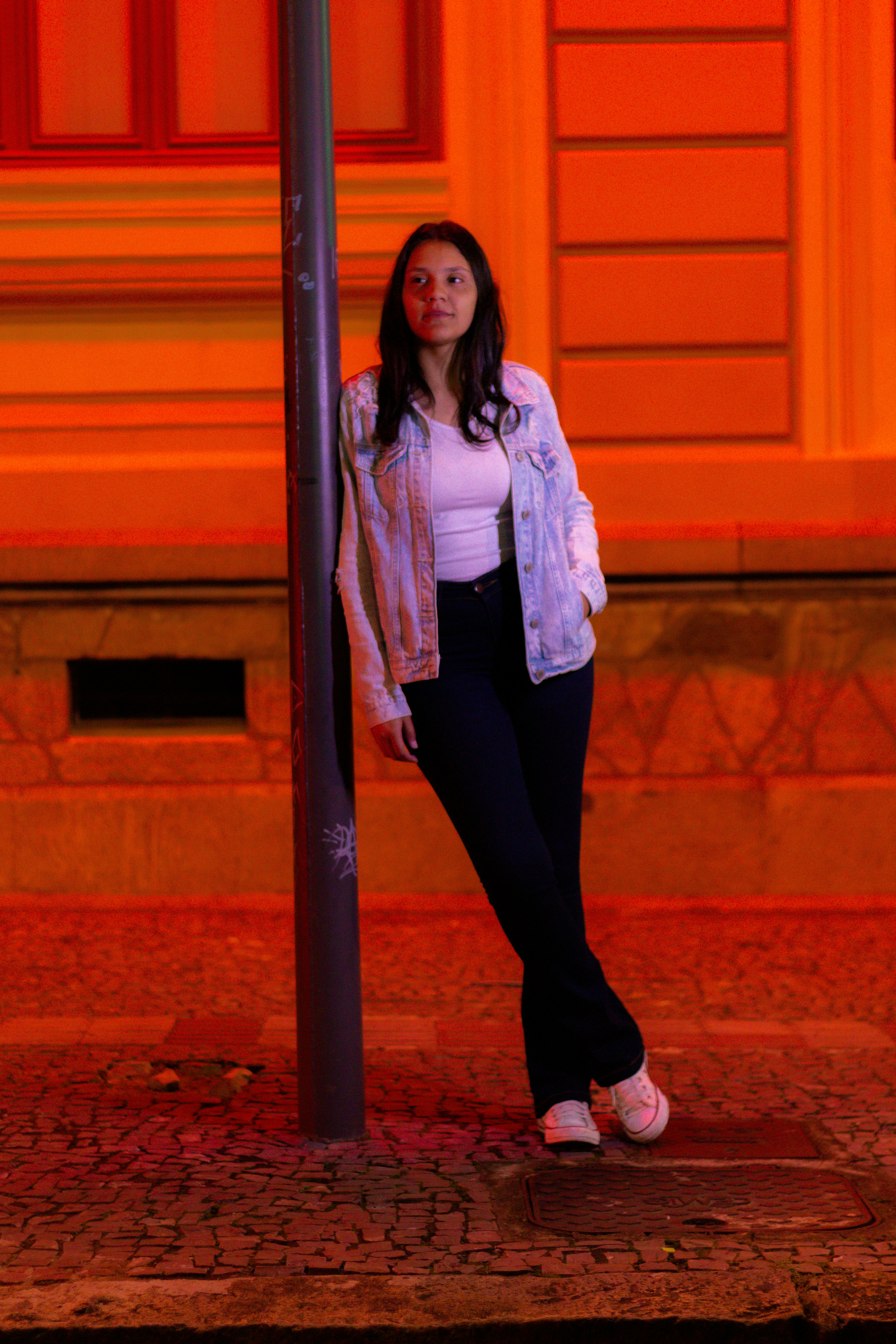 a woman leaning against a pole on a sidewalk