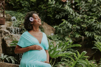 a pregnant woman in a blue dress standing in front of a waterfall