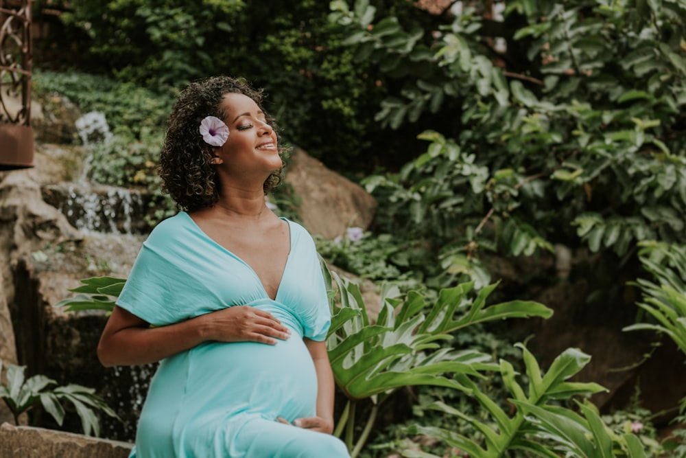 a pregnant woman in a blue dress standing in front of a waterfall