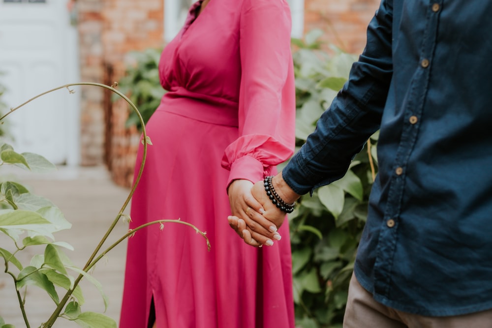 a pregnant woman in a pink dress holding the hand of a man in a blue