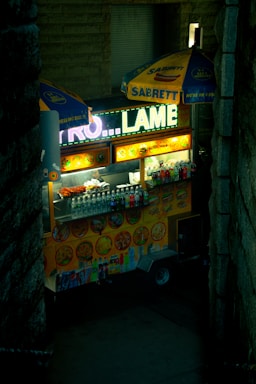 A colorful food cart with various snacks and drinks arranged invitingly in front, bustling with customers.
