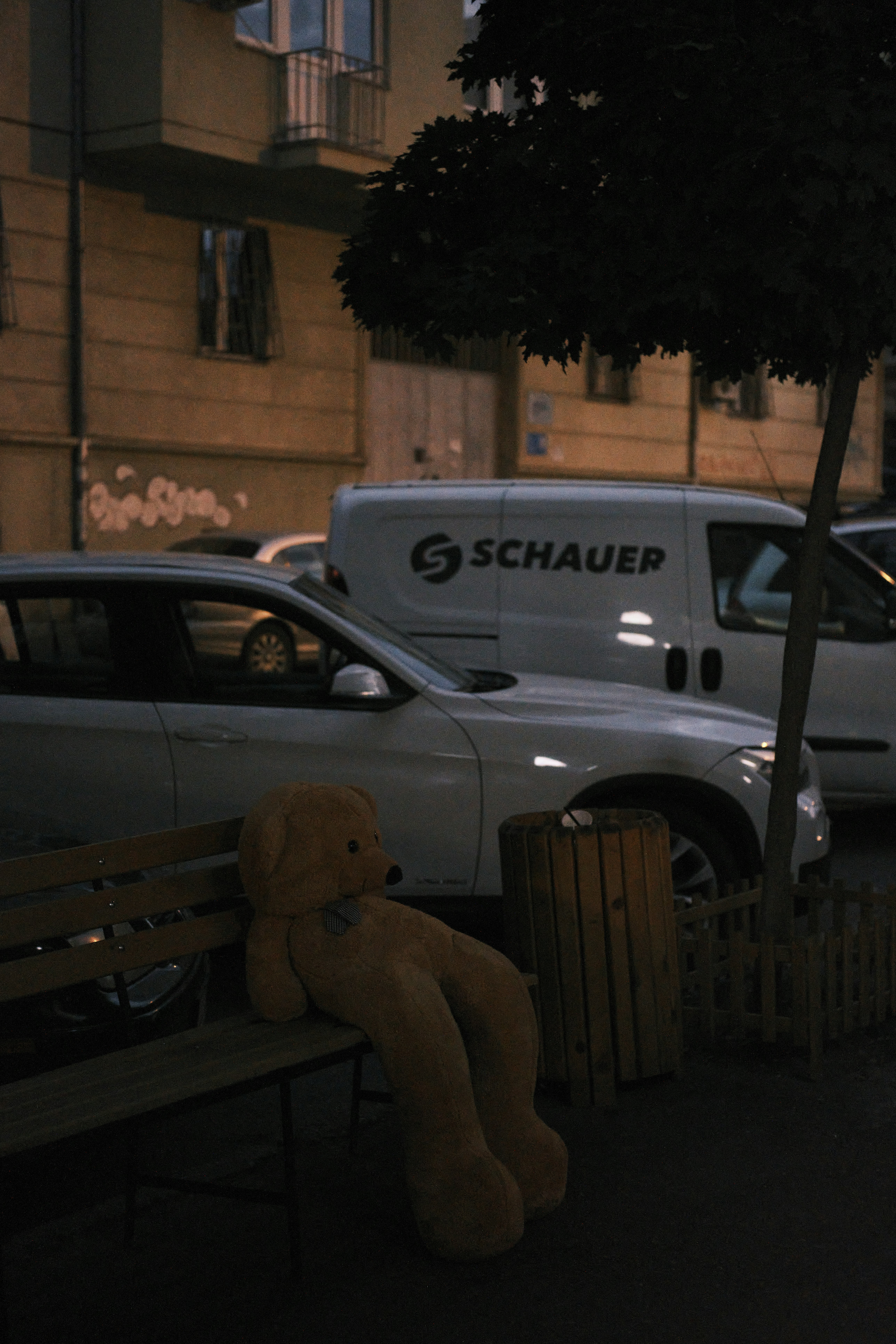 a teddy bear sitting on a bench in a parking lot