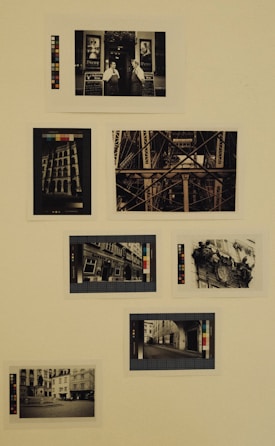 A collection of vintage, sepia-toned photographs displayed on a plain background. Each photo features different urban scenes, including architectural structures and street views. Some images depict people interacting outdoors. Color calibration cards are placed next to the photographs for reference.