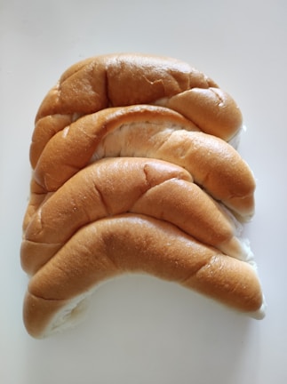 Four soft, golden brown bread rolls are neatly arranged in a slightly overlapping pattern on a white surface.