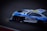 A sleek, high-performance racing car with a vibrant blue and white color scheme is captured in motion on a track. The car features branding logos such as Minerva Oil and Akkodis, and the number 88 is prominently displayed on the side. Design elements suggest it is equipped for professional racing, with aerodynamic features and sponsorship decals visible.