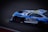 A sleek, high-performance racing car with a vibrant blue and white color scheme is captured in motion on a track. The car features branding logos such as Minerva Oil and Akkodis, and the number 88 is prominently displayed on the side. Design elements suggest it is equipped for professional racing, with aerodynamic features and sponsorship decals visible.