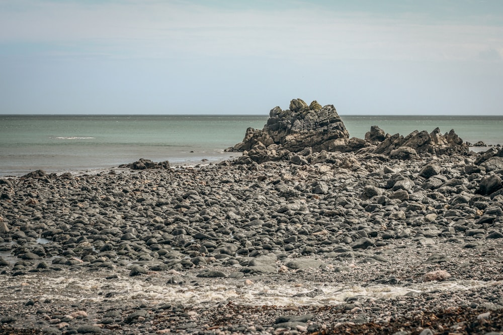 a rock formation on a beach with a body of water in the background