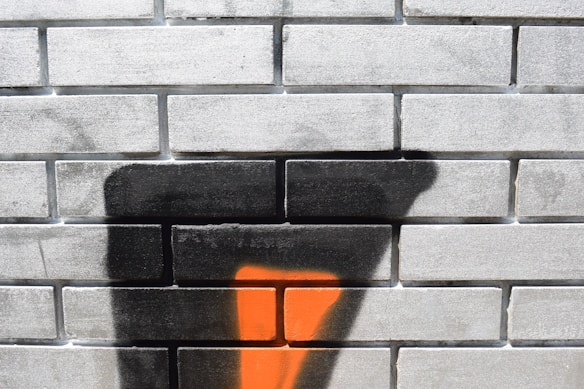 A brick wall decorated with spray paint, featuring abstract shapes in black and orange.