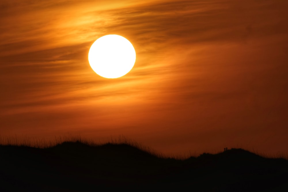 the sun is setting over a grassy hill