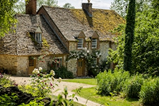 a stone house with a green roof surrounded by greenery