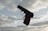 A handgun with a brown grip and black body is pictured against a backdrop of a cloudy sky. The focus is on the firearm with details of its hammer, trigger, and barrel clearly visible.