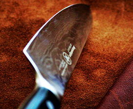 Close-up of a Damascus knife blade with intricate patterns, set against a black and gold background.