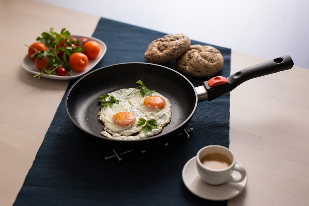 a frying pan filled with eggs next to a cup of coffee