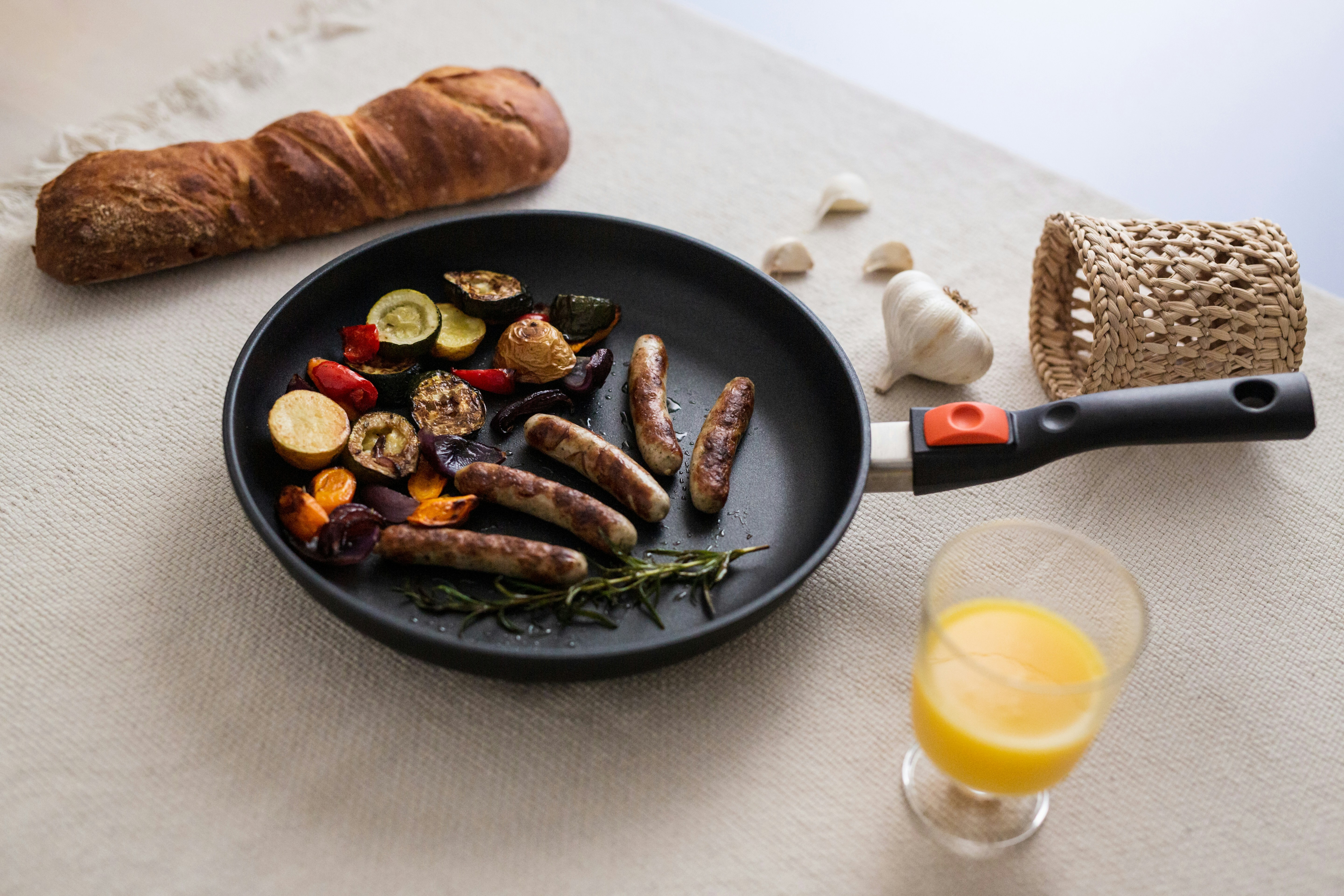 a plate of sausages and vegetables next to a glass of orange juice