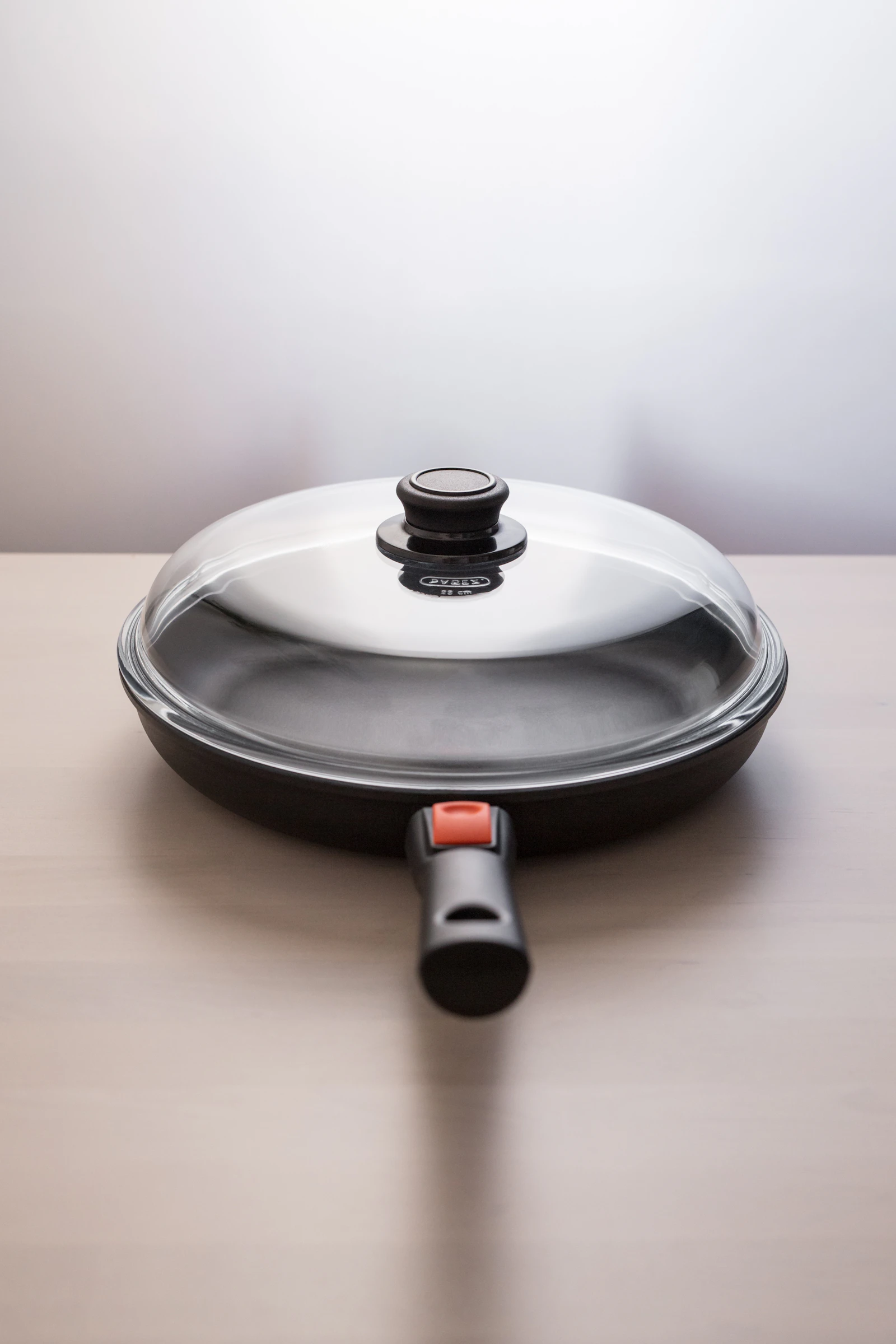 A frying pan with a lid on a wooden surface