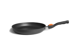 A black frying pan with an orange detail on the handle is placed against a plain, light-colored background. The pan has a sleek, modern design with a smooth, non-stick surface.