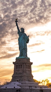 the statue of liberty is silhouetted against a cloudy sky