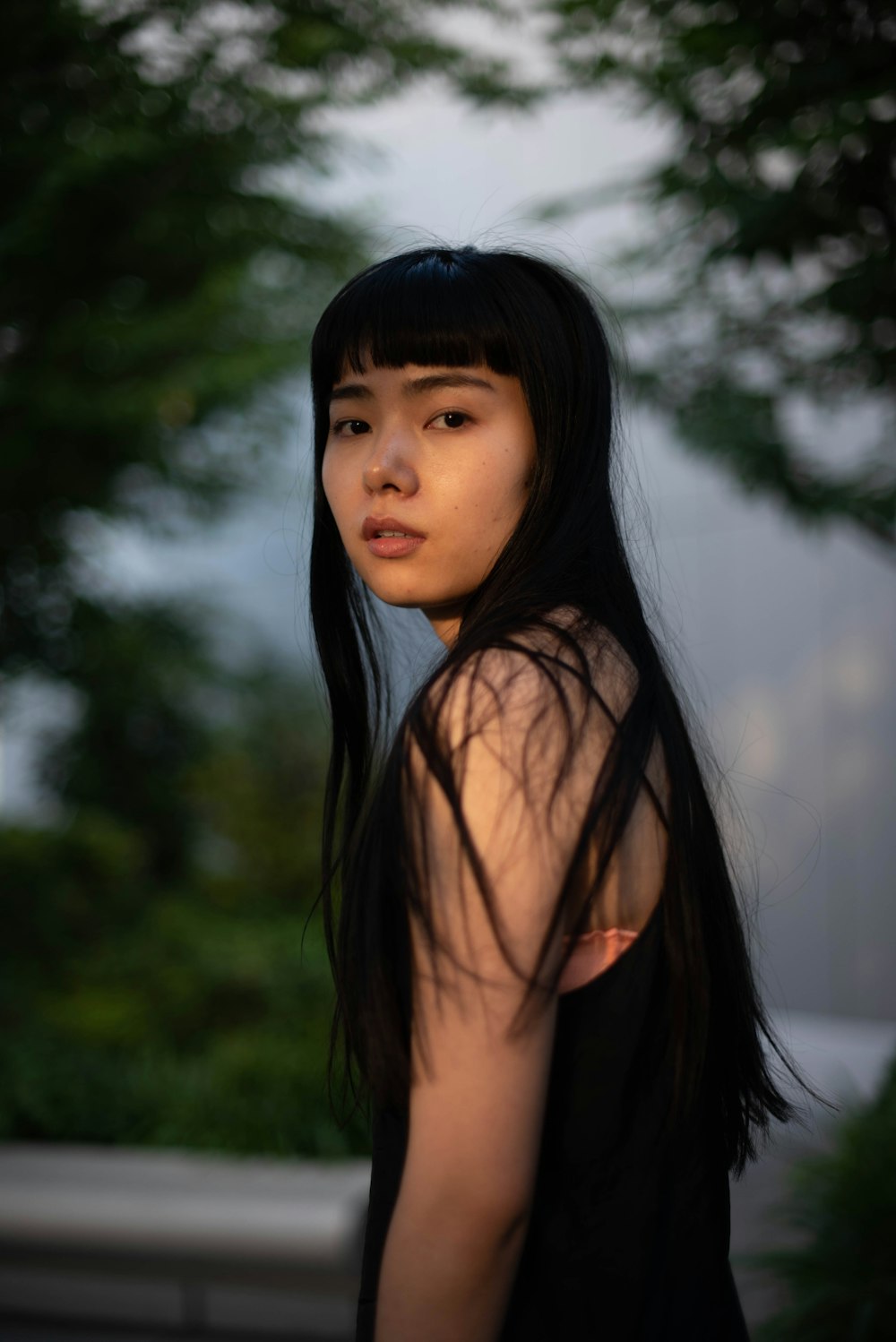 a woman with long black hair standing in front of a tree