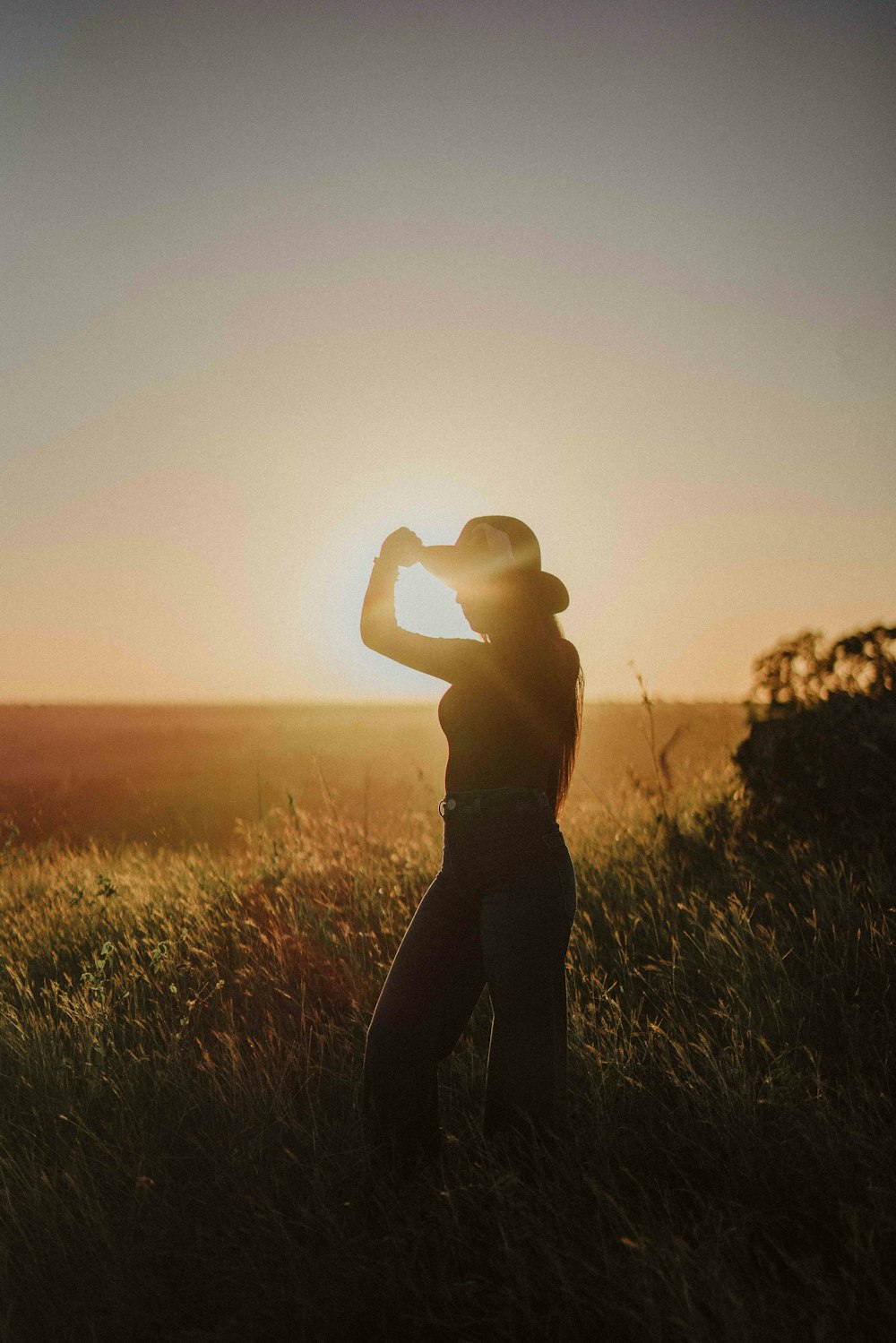 a woman standing in a field at sunset