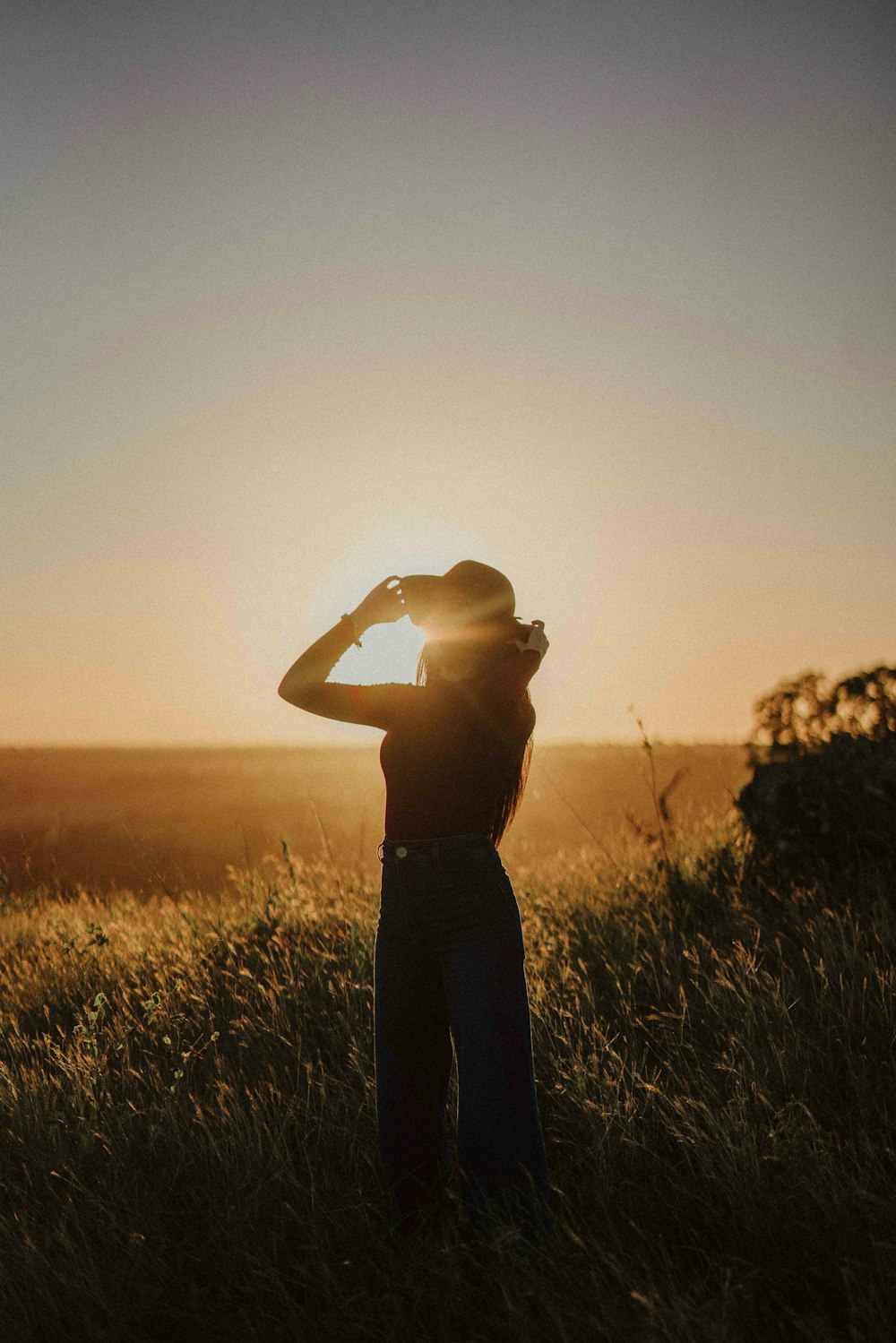 a woman standing in a field at sunset