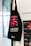 A black tote bag hangs on a wall featuring a colorful abstract design of red and purple shapes. The text on the bag reads 'DeSIGN DEPARTMENT' with additional information at the bottom. The background includes part of a white poster with text and a partial view of a window.