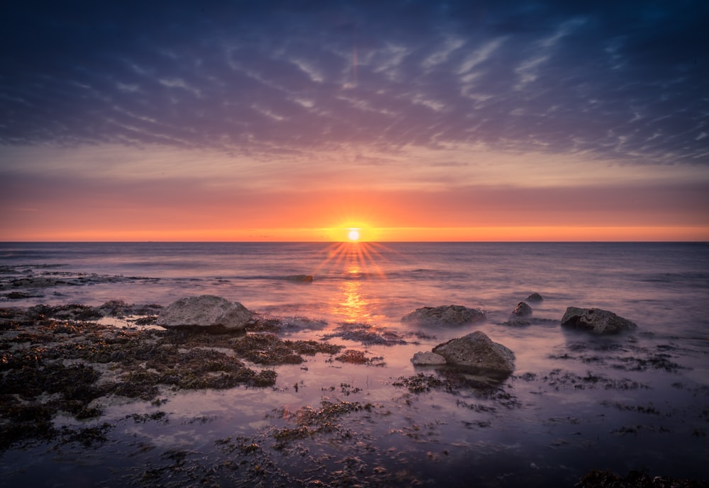 a sunset over the ocean with rocks in the foreground