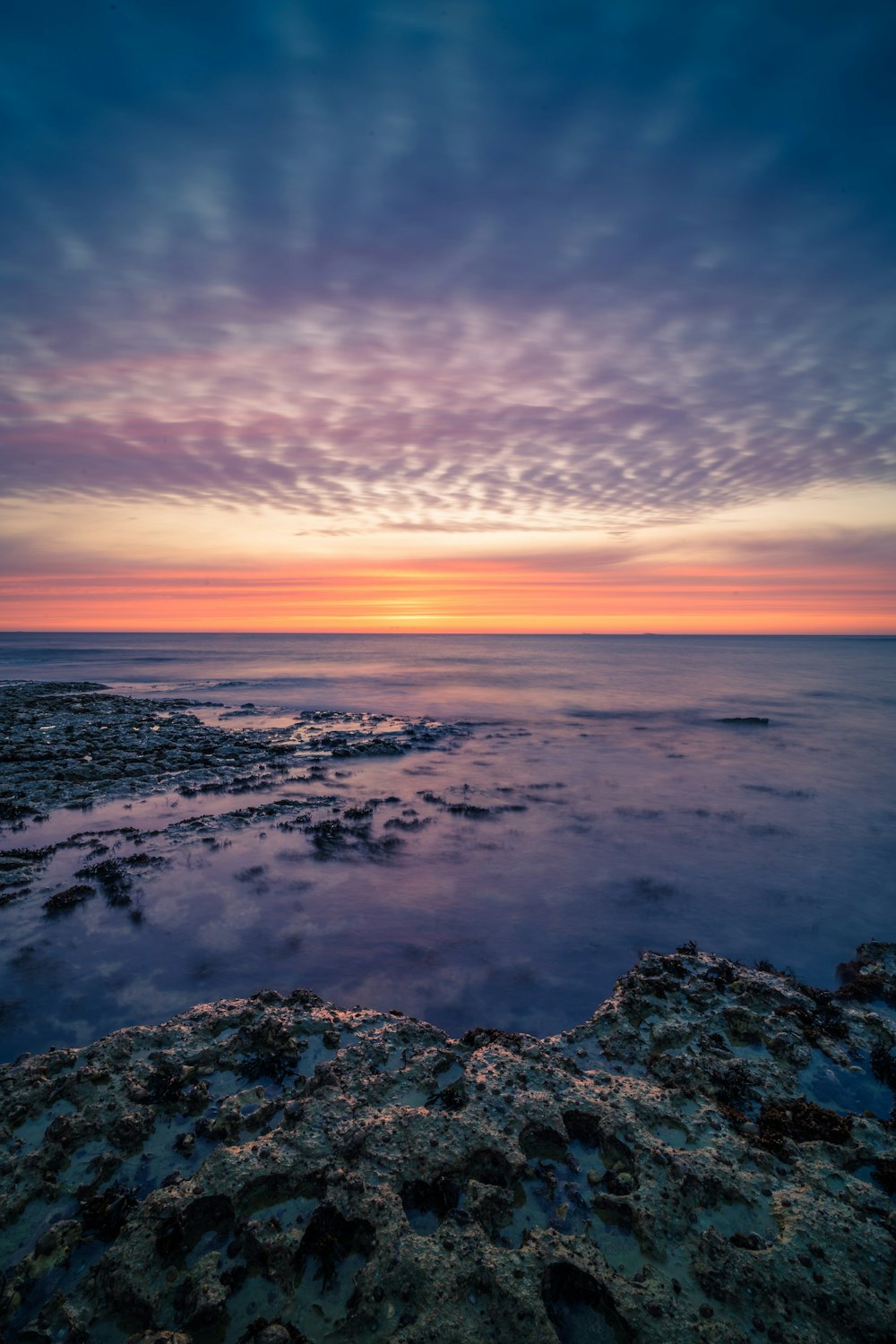 the sun is setting over the ocean on a cloudy day