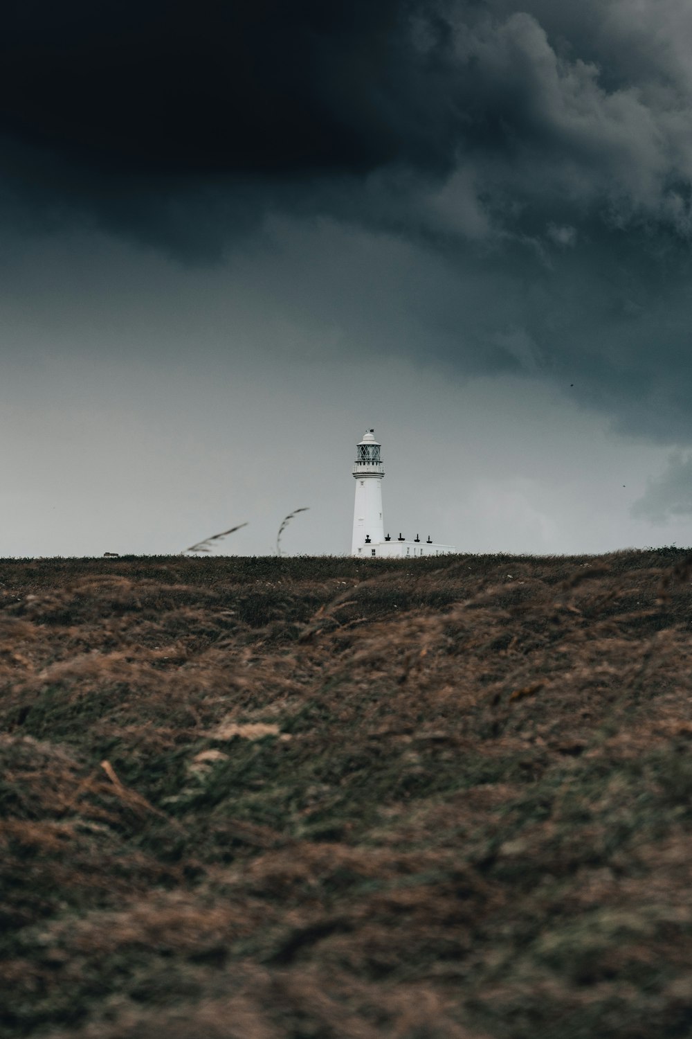 a white light house on a hill under a cloudy sky