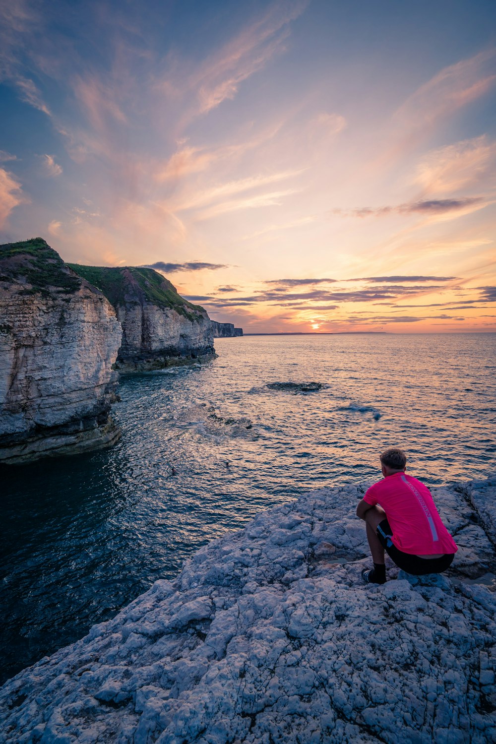 a man sitting on a rock looking out at the ocean