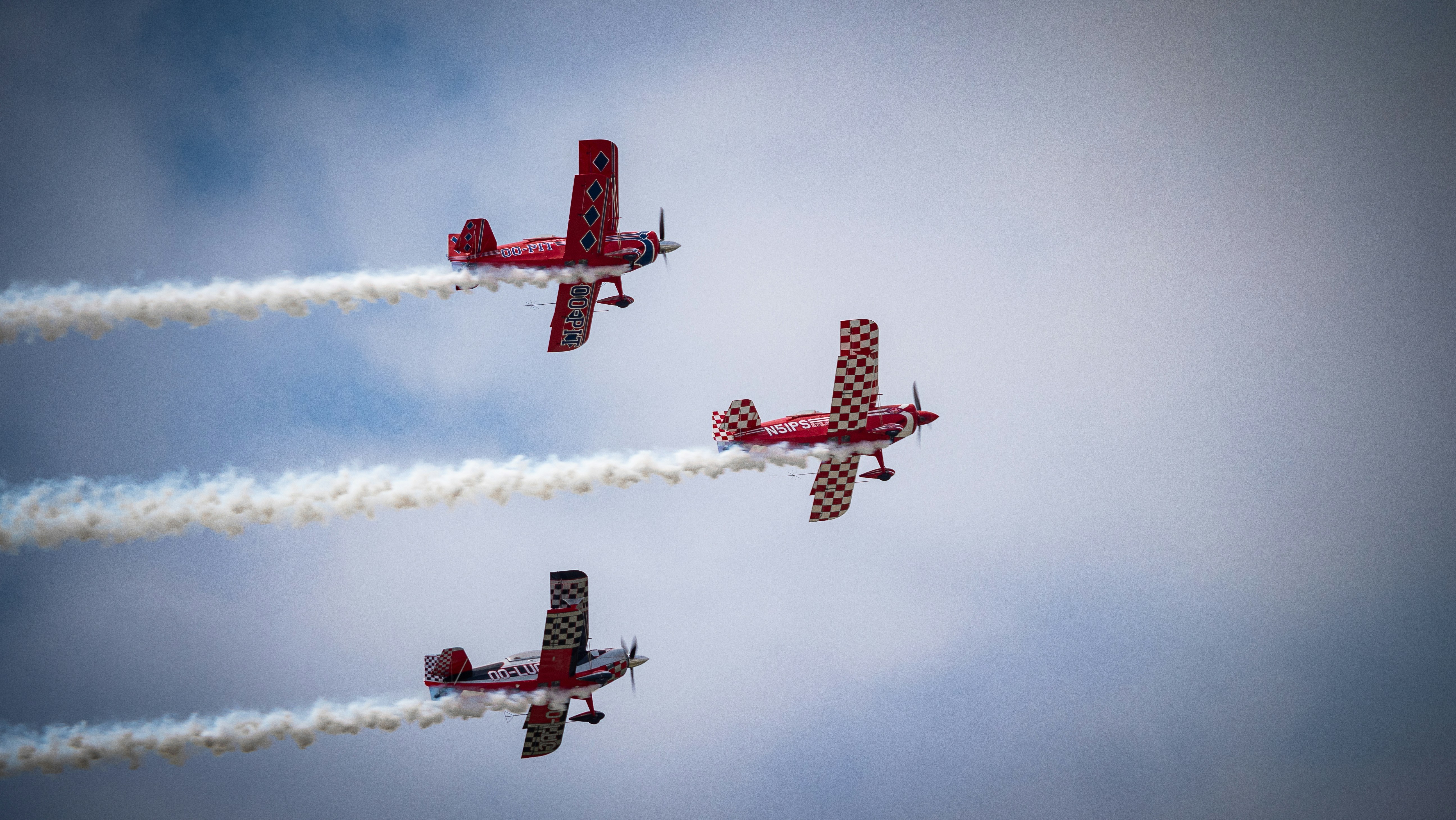 three red airplanes flying in formation with smoke trailing behind them