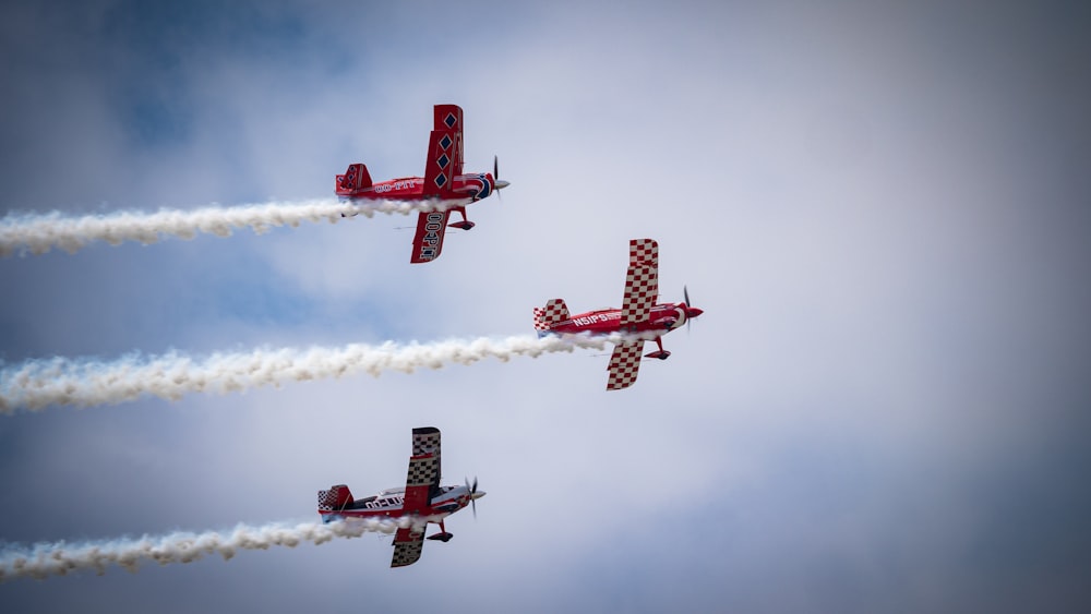 three red airplanes flying in formation with smoke trailing behind them