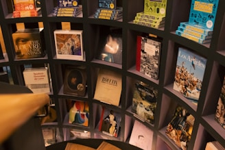 A bookshelf with various books displayed in a grid-like structure. The books have diverse covers, including topics on art, history, economy, and more. The shelf is part of an interior with a wooden railing visible in the foreground.