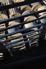 A view from above shows large wooden cable reels stacked together, partially obscured by a metal grid structure in the foreground.