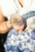 Hands holding a delicate jar of cream with a blurred natural background.