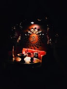 An intricately designed wooden panel with a central Om symbol is illuminated softly. Below, a small altar setup includes a lit oil lamp, a brass plate, and various religious artifacts, creating a serene and spiritual atmosphere.
