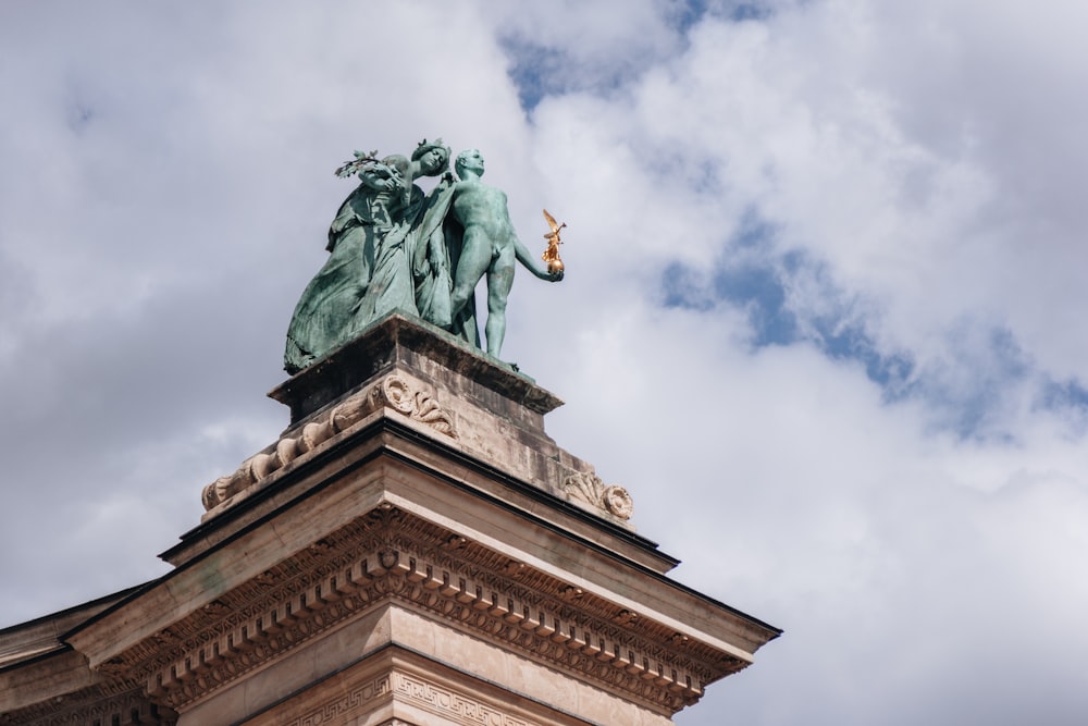 Una estatua en la parte superior de un edificio con nubes en el fondo