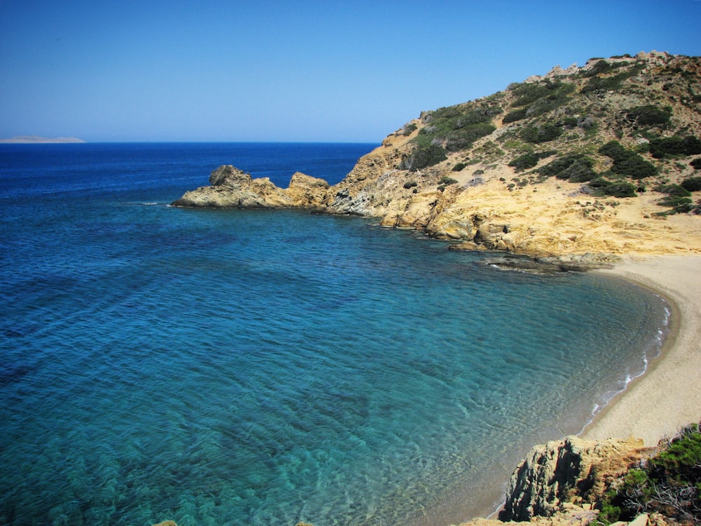 a beach with clear blue water next to a cliff