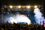 A panoramic view of a packed concert venue with vibrant light beams cutting through the smoke.