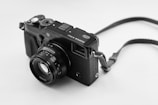 A classic camera with a textured body, featuring a prominent lens and various control dials. The camera strap is attached, and the image is captured in black and white.