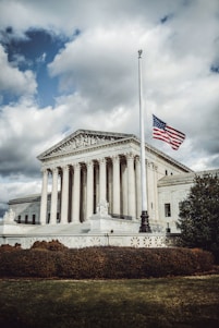 A stately, classic building with an American flag gently waving in front under a clear sky.