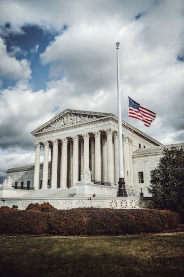 A stately, classic building with an American flag gently waving in front under a clear sky.